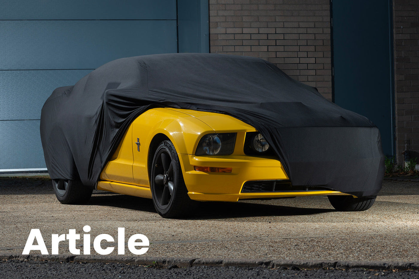 Yellow ford mustang outside with a black indoor car cover over the top showing the front of the car 